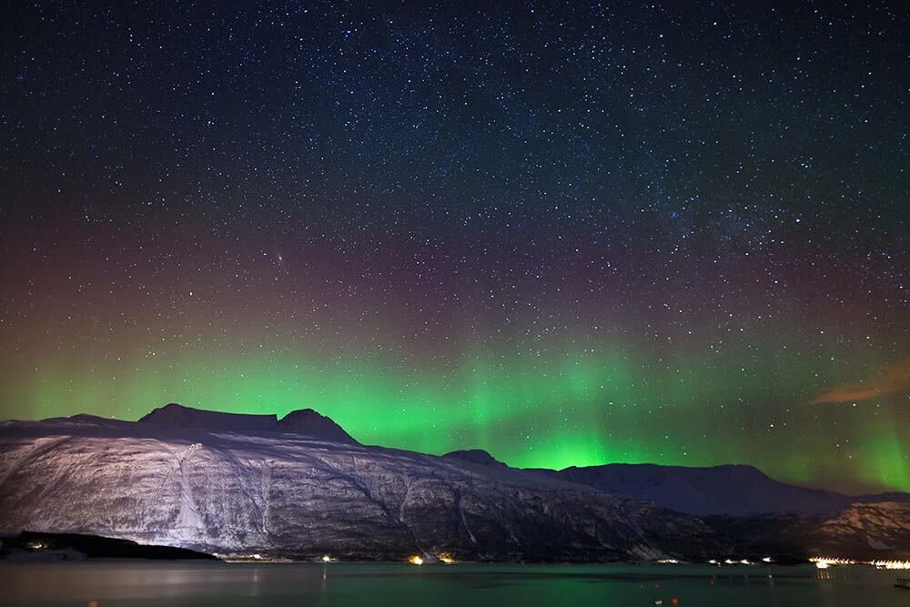 Arctic night in the surroundings of Tromso, Norway : northern lights rising beyond a fjord, enlightening a sky full of stars